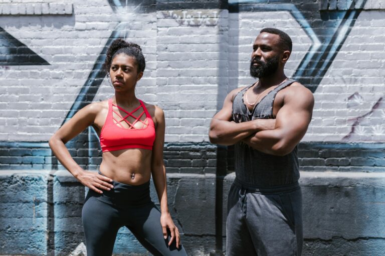 A fit man and woman pose confidently against a graffiti wall, embodying active lifestyle.